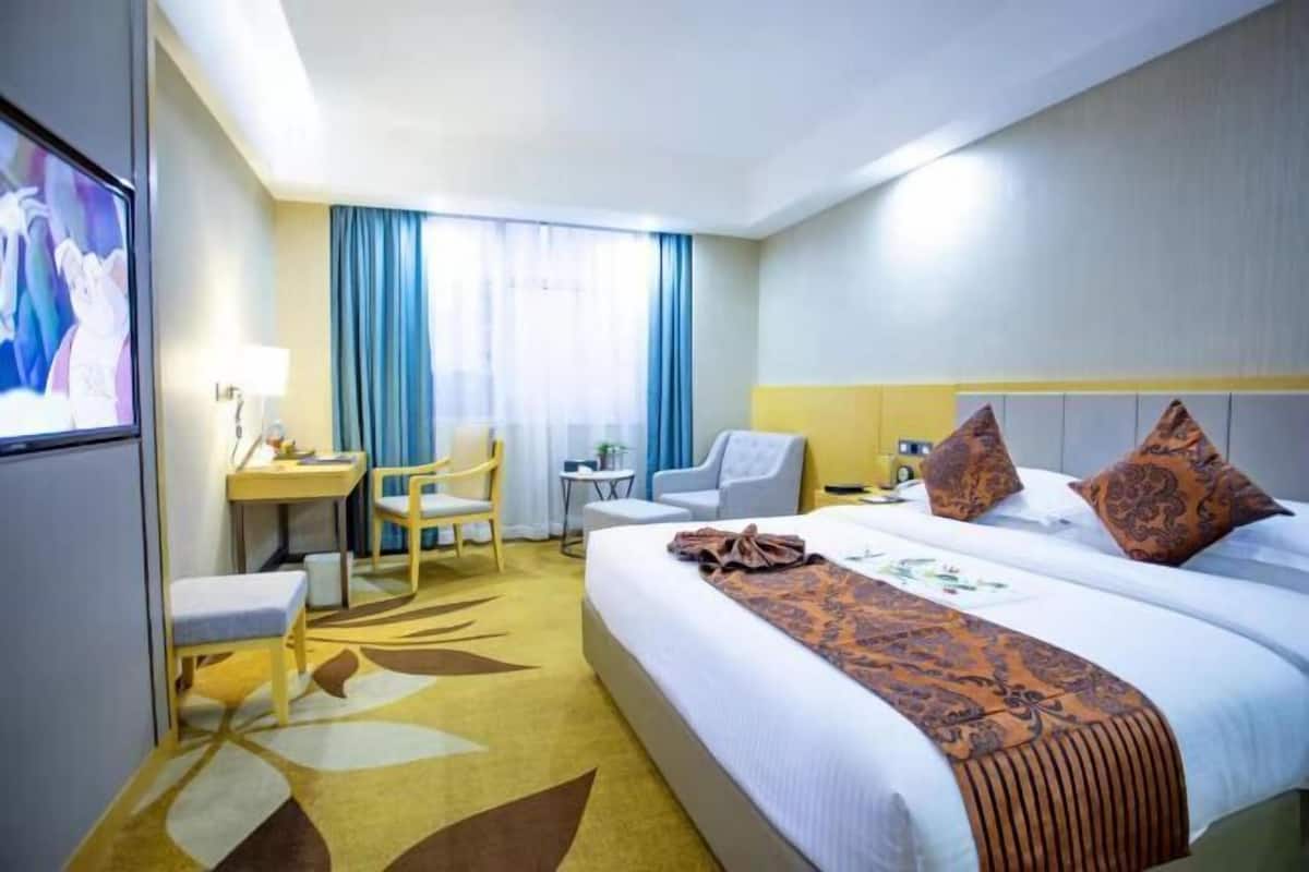 Ein Hotelzimmer mit einem großen Bett, einem Schreibtisch, einem Stuhl, einem Fernseher und einem Fenster mit Vorhängen.