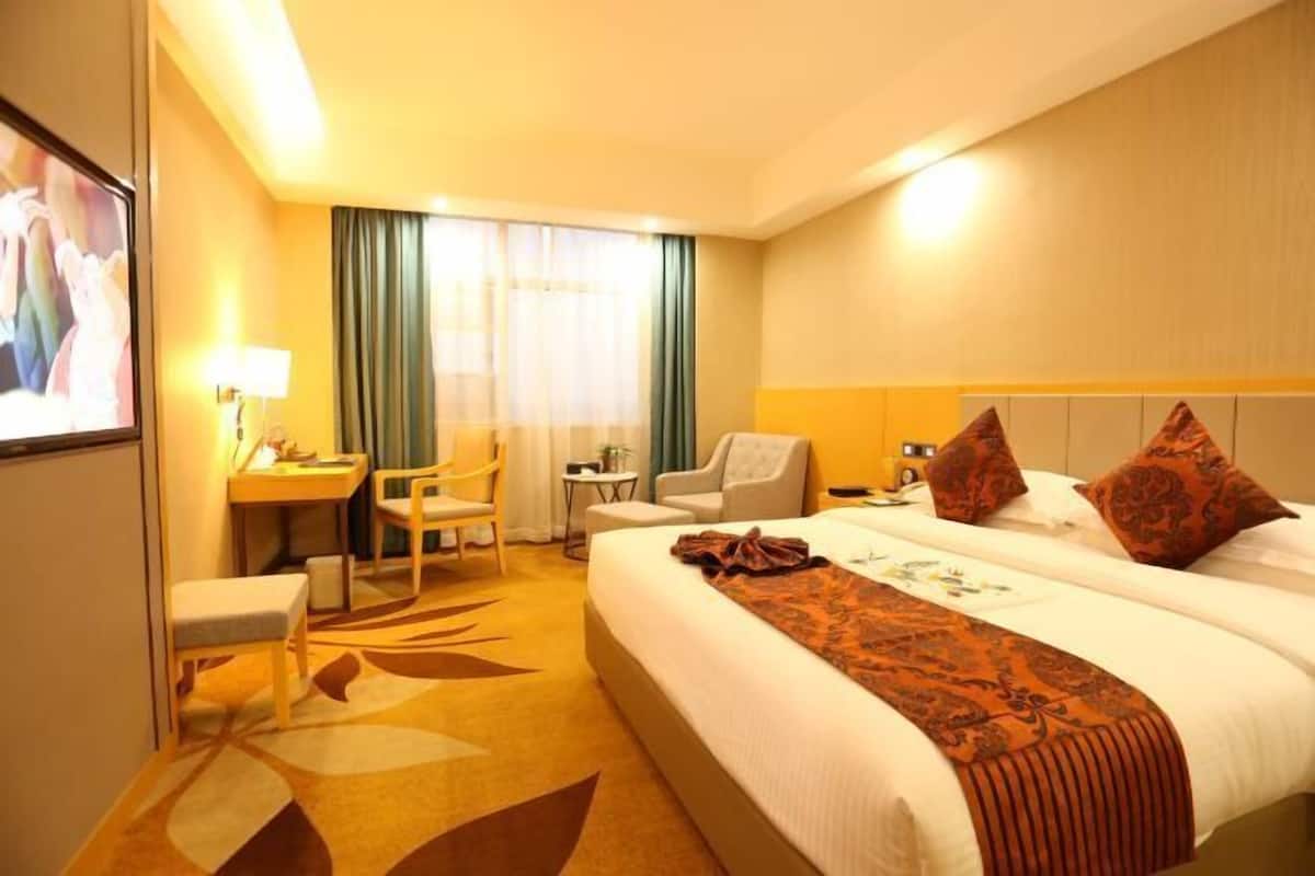 Ein Hotelzimmer mit einem großen Bett, einem Schreibtisch, zwei Stühlen, einem Fernseher und einem Fenster mit Vorhängen.