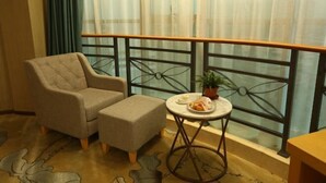 Un balcon avec un fauteuil rembourré, une petite table sur laquelle se trouve une assiette de nourriture et une plante en pot.