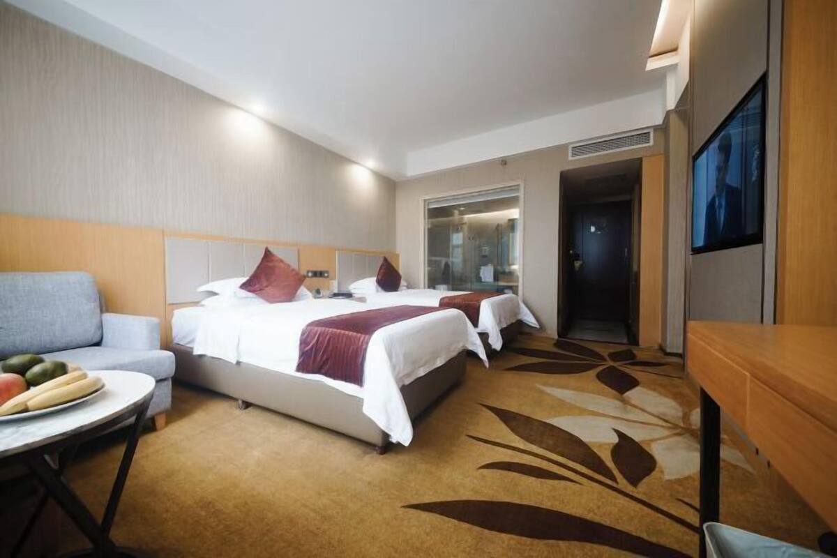 Ein Hotelzimmer mit zwei Betten, einem Sofa, einem Esstisch und einem Fernseher.
