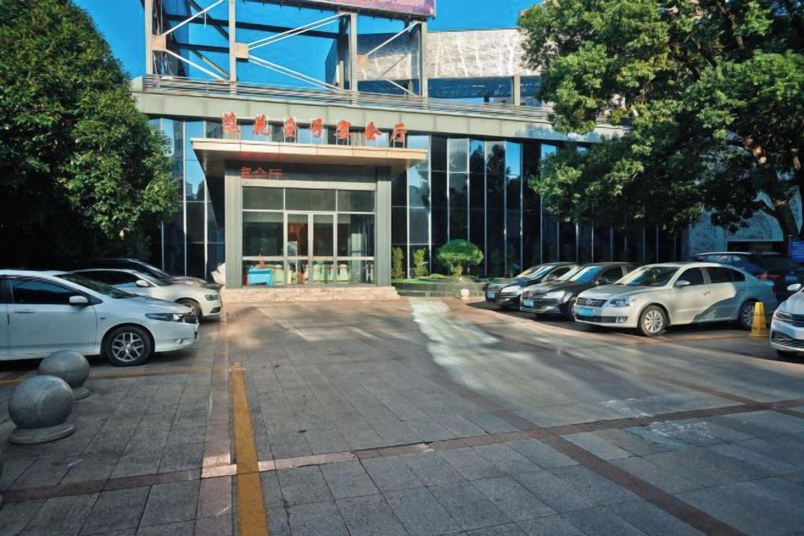 A building with a modern entrance, a parking lot with several cars, and a clear sky.