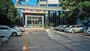 A building with a modern entrance, a parking lot with several cars, and a clear sky.