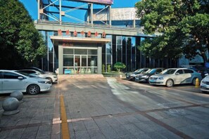 Een gebouw met een moderne ingang, een parkeerplaats met meerdere auto's, en een heldere lucht.
