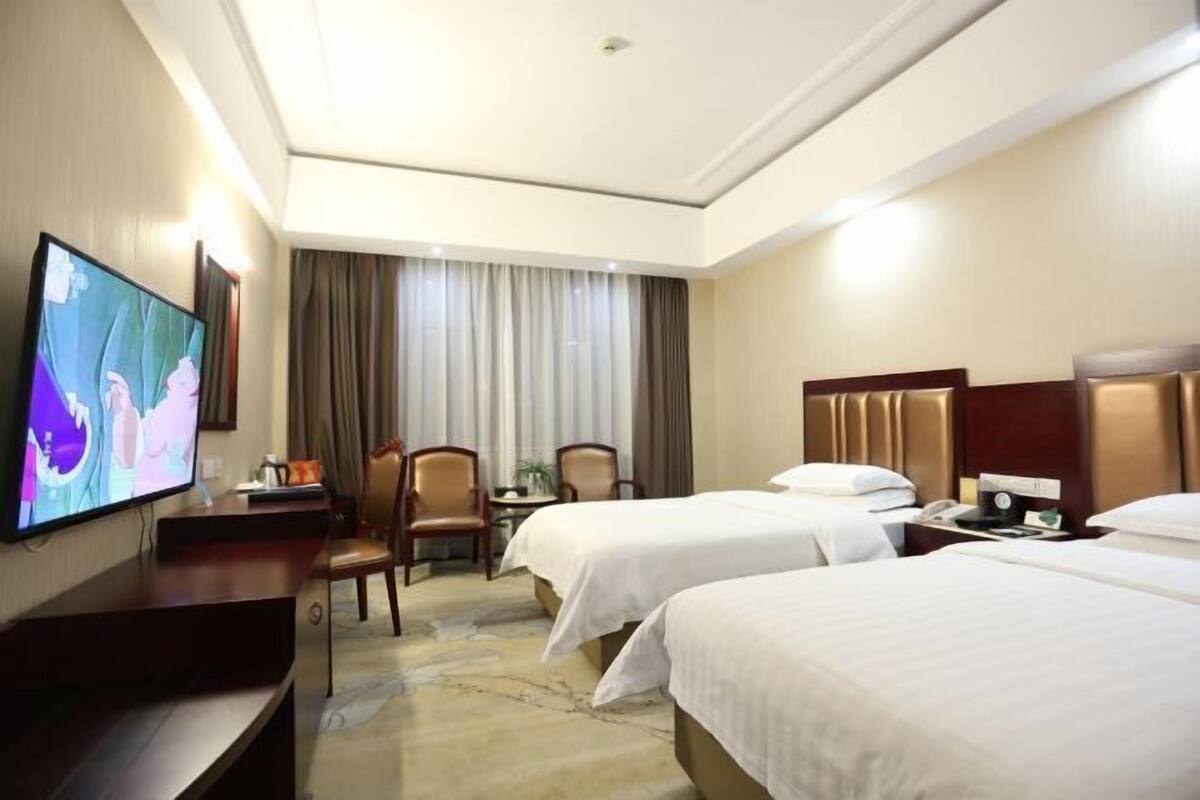 Ein Hotelzimmer mit zwei Betten, einem Fernseher, einem Schreibtisch und einem Sessel.