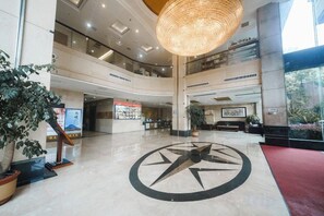 Een ruime lobby met een centrale klok, hoge plafonds en een grote hanglamp.