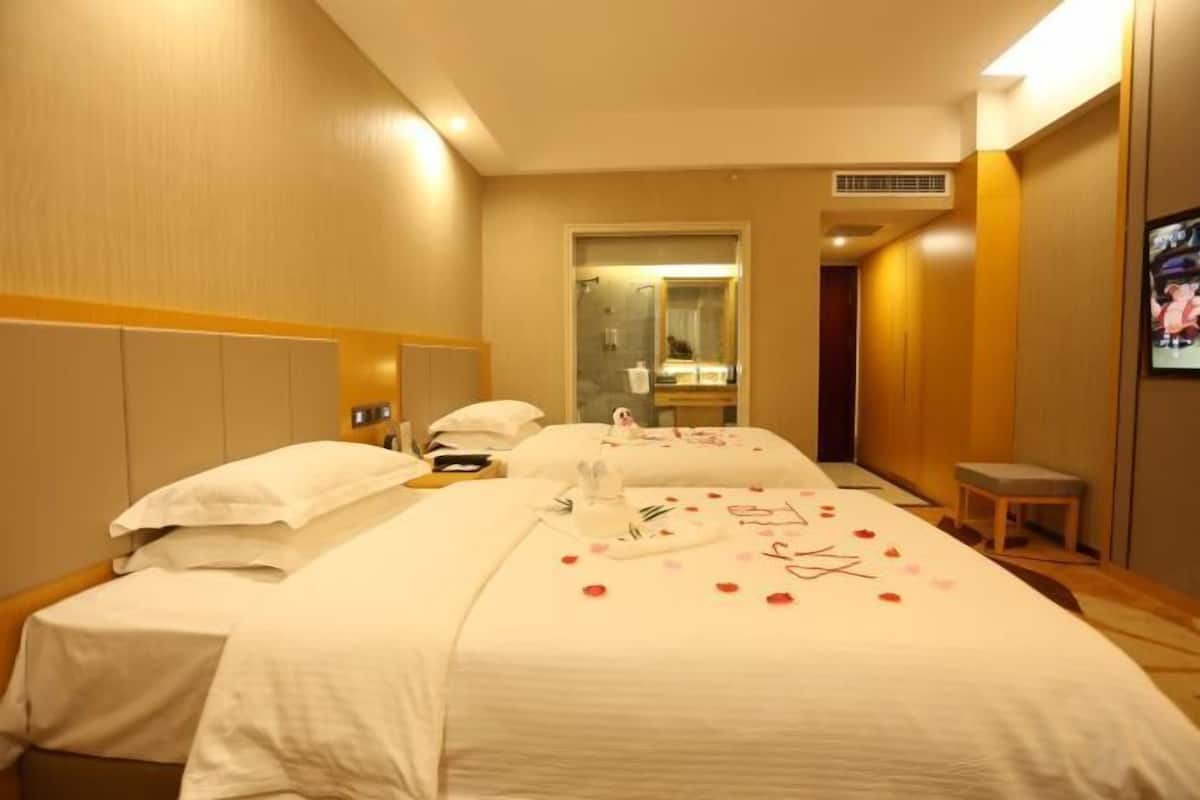 Ein Hotelzimmer mit zwei Betten, einem kleinen Tisch, einem Stuhl und einem an der Wand befestigten Fernseher.