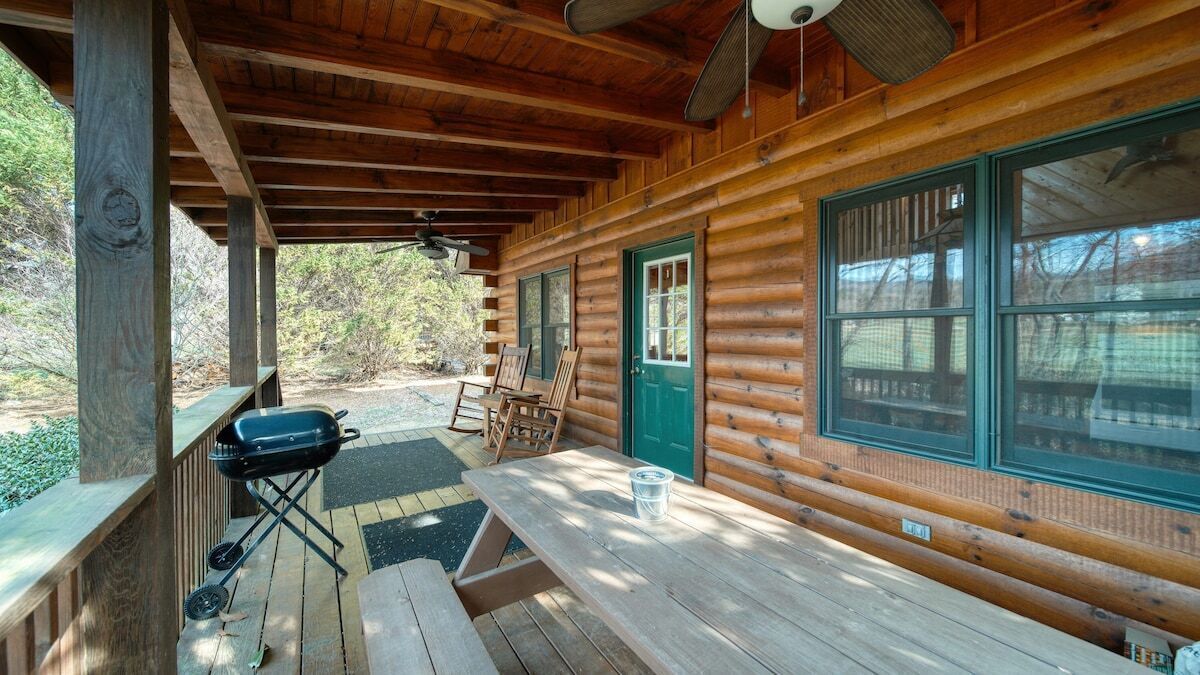 Una baita di legno con veranda coperta, un barbecue e un tavolo da picnic.