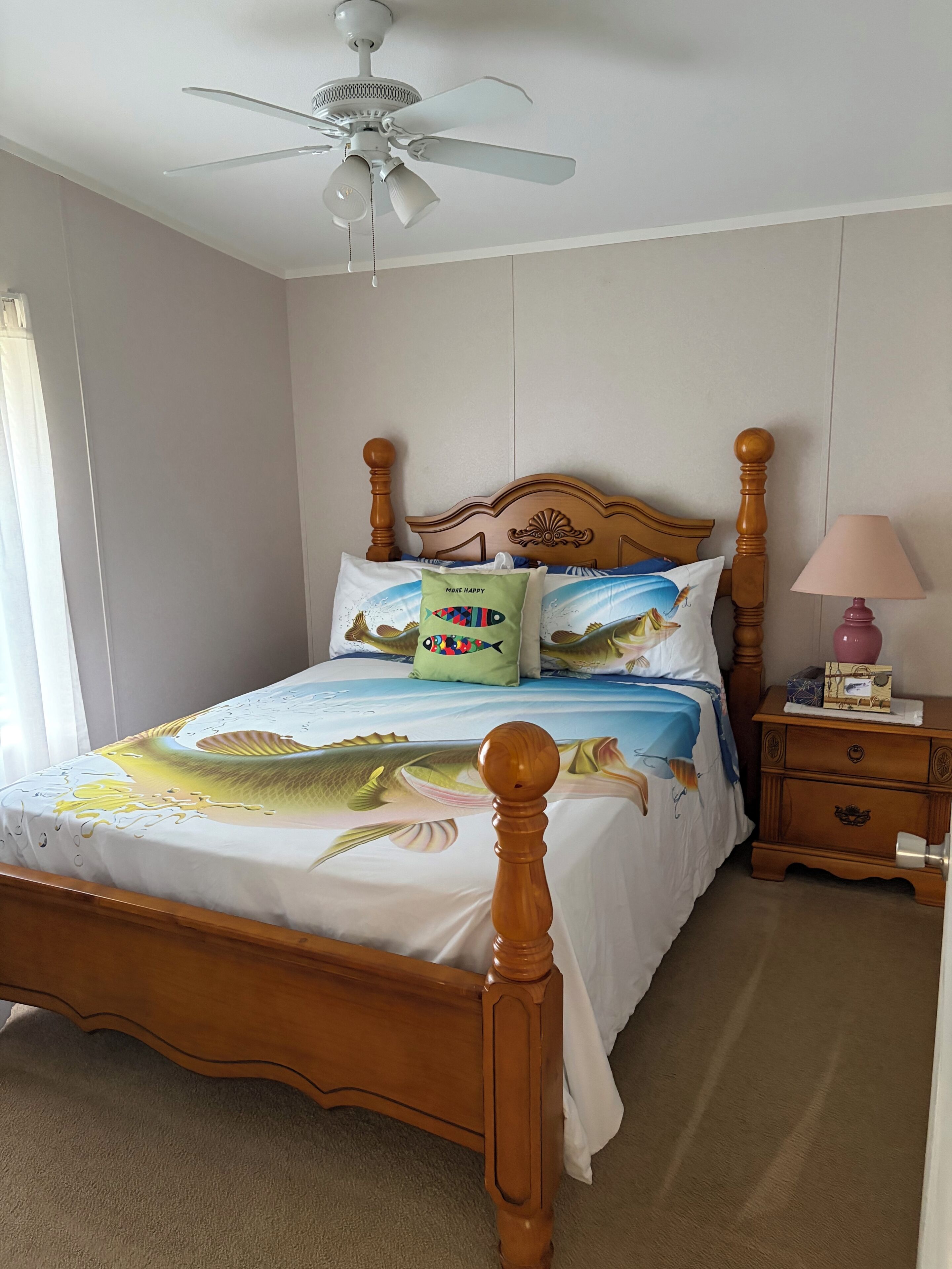 A bedroom with a wooden bed, a ceiling fan, a nightstand, and a lamp.