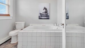 A bathroom with a white toilet, a bathtub, and a wall-mounted picture of a horse in a bathtub.