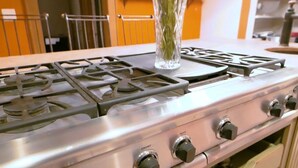 A kitchen with a gas stove, a vase, and a chair.