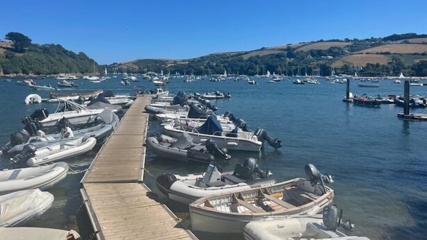 A marina with several boats docked at wooden piers, surrounded by hills and clear blue skies.