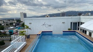 Piscina no terraço com vista para a cidade e montanhas ao fundo.