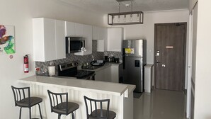 Uma cozinha moderna com armários brancos, uma geladeira de aço inoxidável, micro-ondas e um balcão com três banquetas.