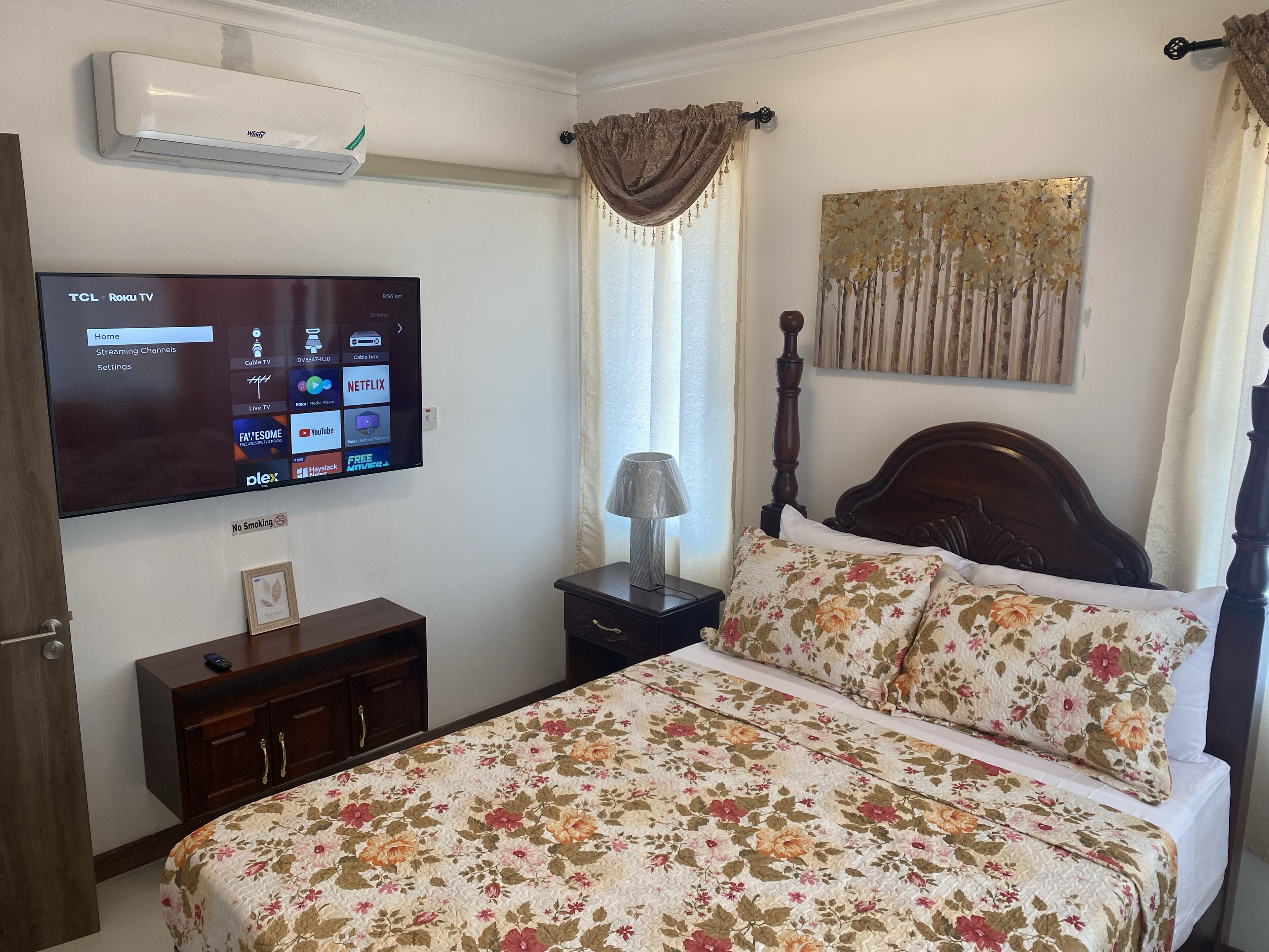 A bedroom with a bed, a TV mounted on the wall, a bedside table with a lamp, and a painting on the wall.