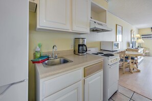 A compact kitchen with white cabinets, a sink, a stove, a coffee maker, and a dining area with a table and chairs.