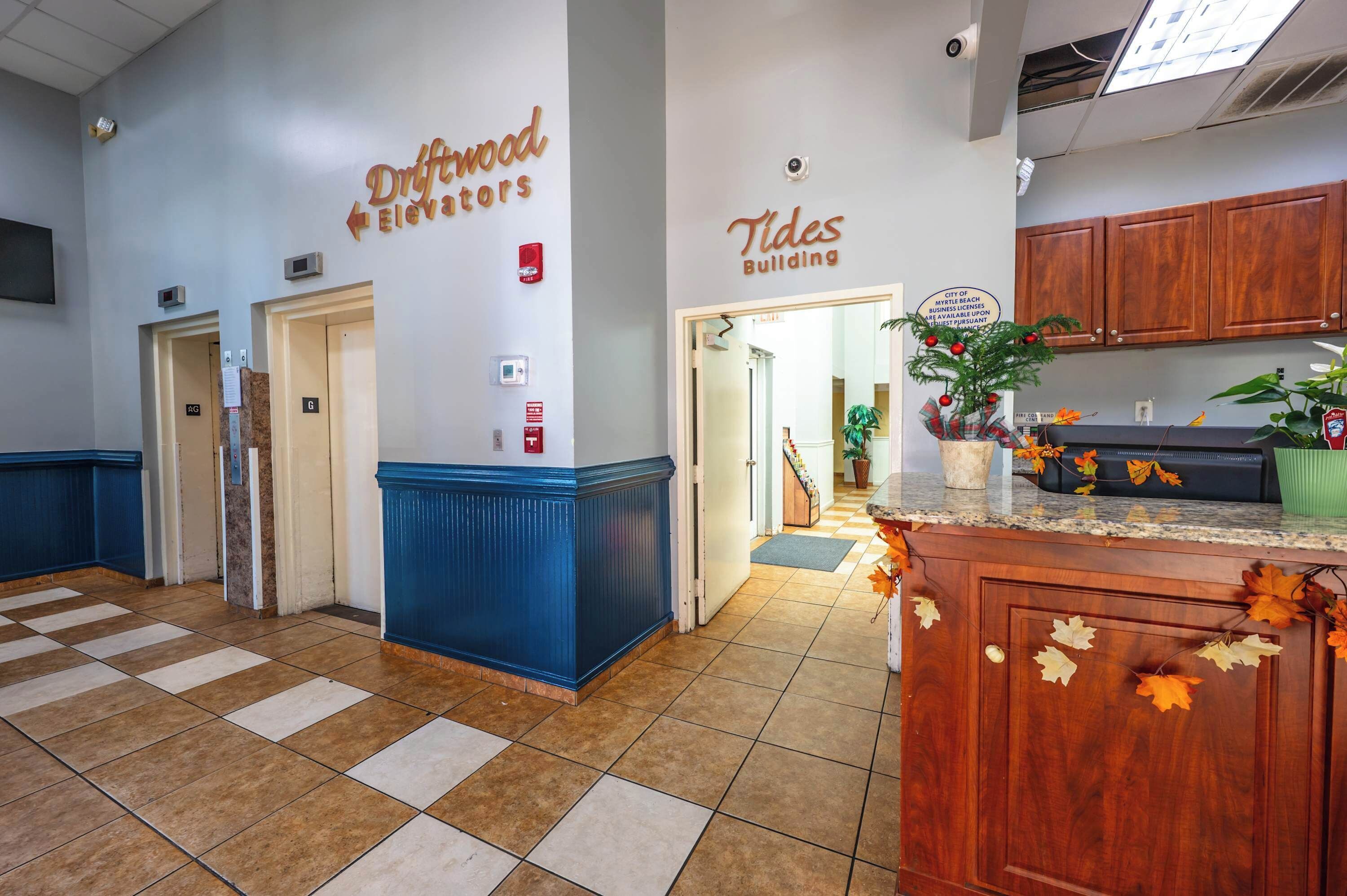 A hotel lobby with a checkered floor, a reception desk, and signs for 'Driftwood Elevators' and 'Tides Building'.