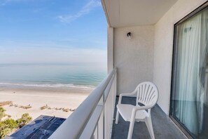 A balcony with a white chair and a view of the beach.