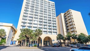 A multi-story hotel with a central entrance, surrounded by palm trees, and featuring balconies on each floor. - Beautiful High-Floor - Ocean Views Newly Renovated (Myrtle Beach)
