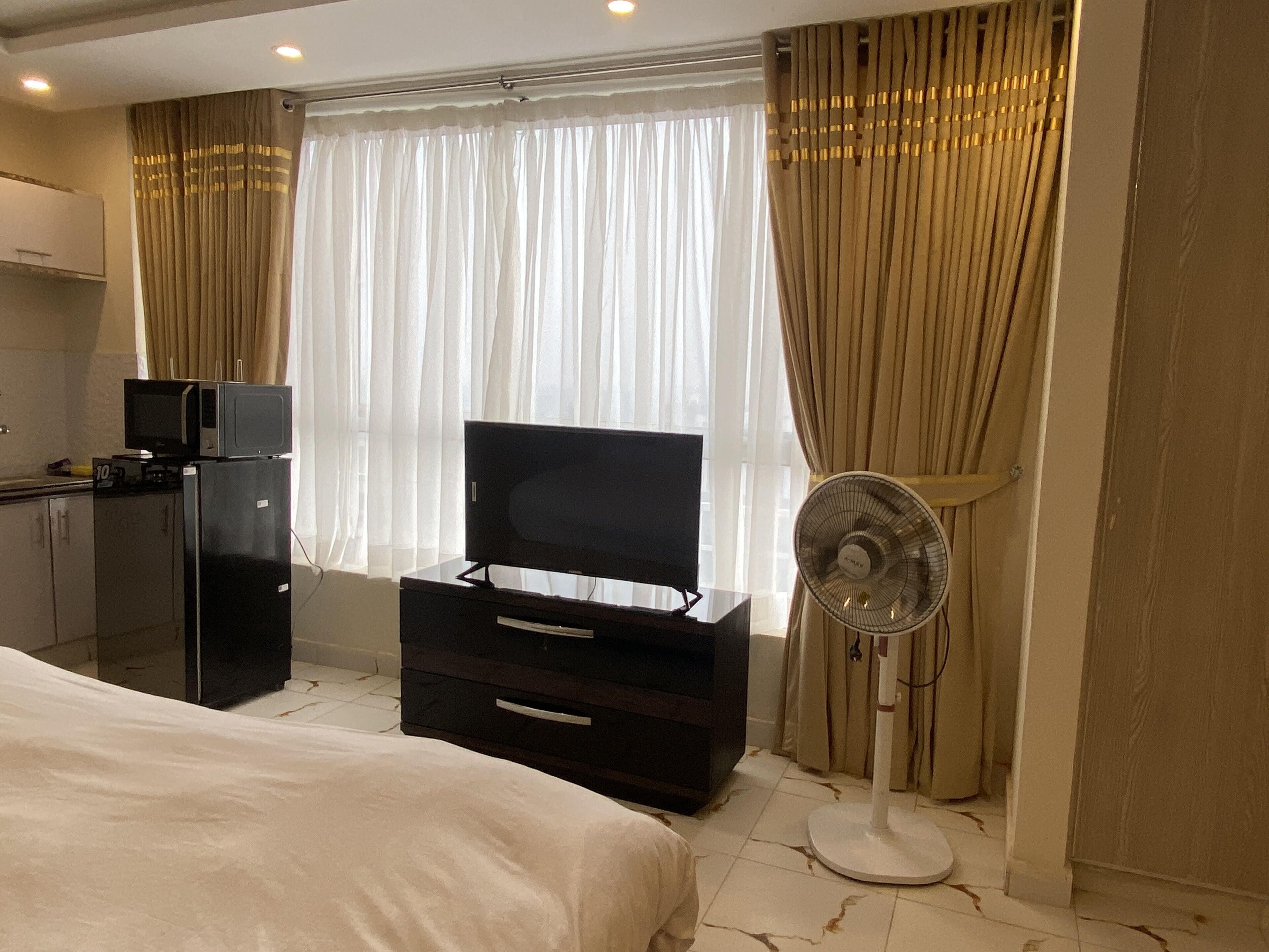 Ein Hotelzimmer mit einem Bett, einem Fernseher auf einer Kommode, einem Kühlschrank, einer Mikrowelle, einem Ventilator und einem Fenster mit Vorhängen.