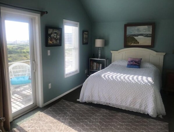 A bedroom with a bed, a window, a door, and a view of the outdoors.