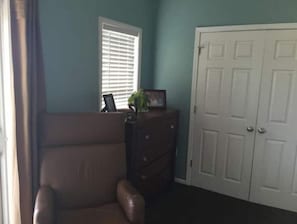 A room with teal walls, a brown leather chair, a wooden dresser, and a white door.