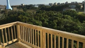 Um deck de madeira com vista para uma área residencial e uma estrutura azul alta ao longe.