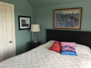 A bedroom with a bed, a nightstand, a lamp, and two framed pictures on the wall.