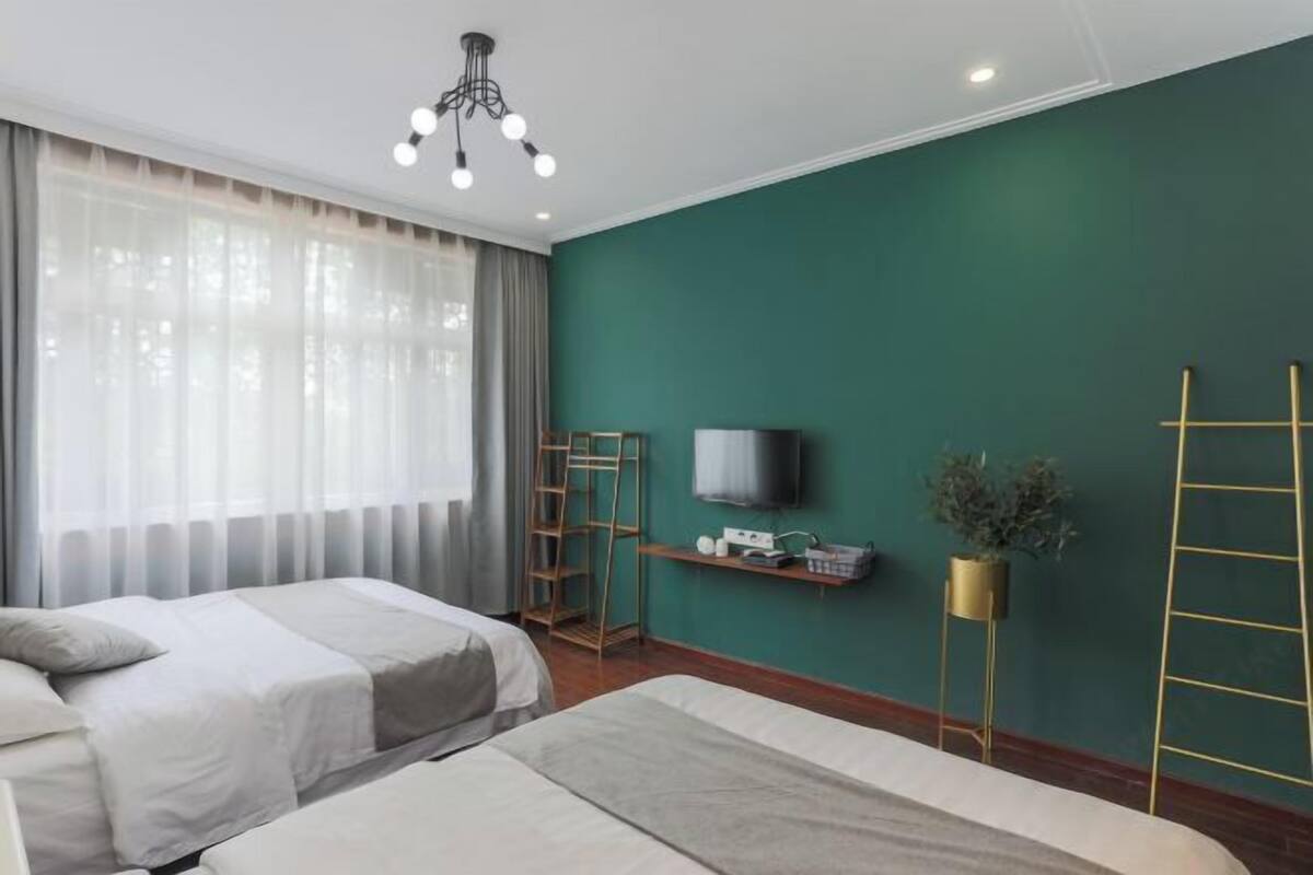A hotel room with two beds, a TV, a shelf with items, and a green wall.