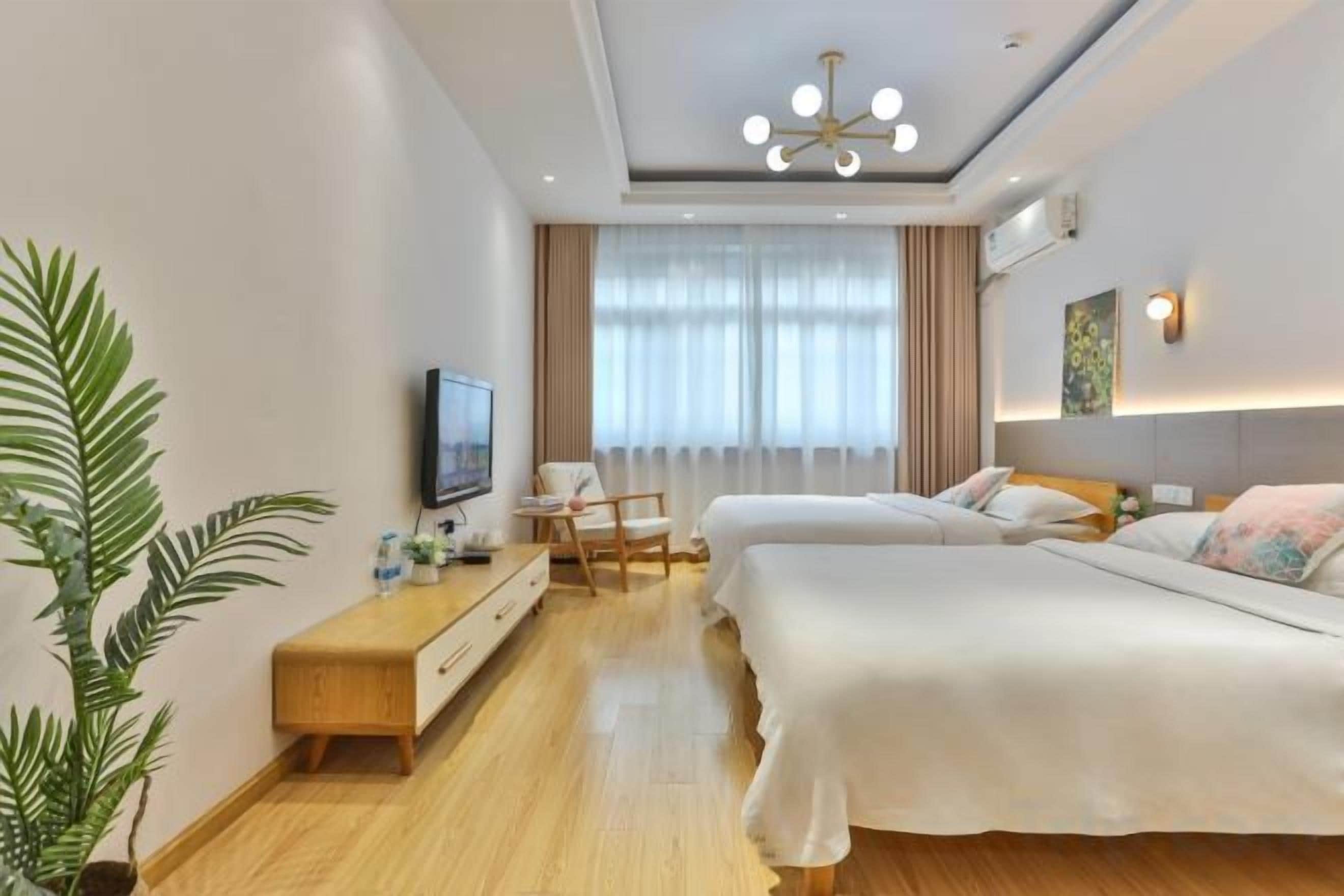 A hotel room with two beds, a TV, a desk, and a large window with curtains.