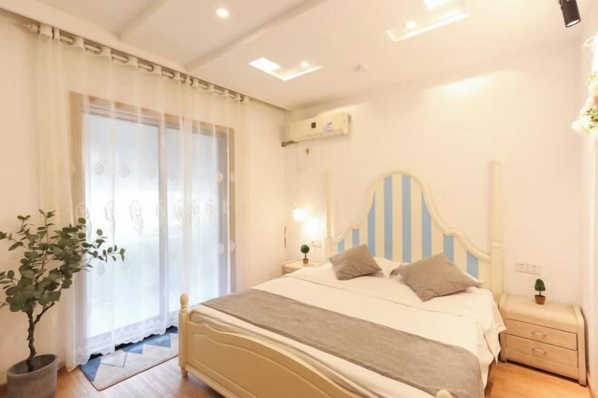 A bedroom with a bed, bedside tables, a potted plant, and a window with curtains.