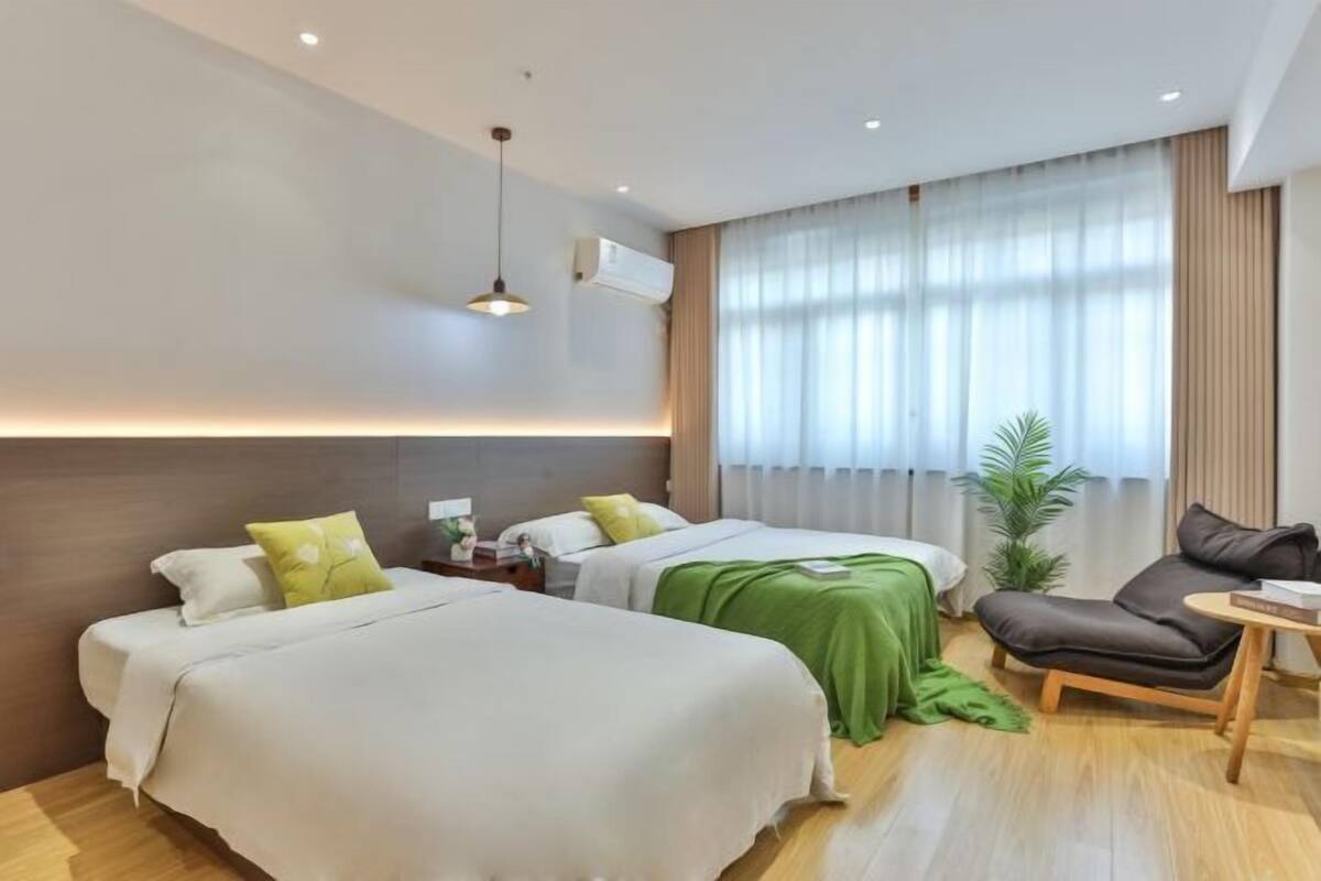 A modern hotel room with two beds, a green throw blanket, a brown leather chair, and a small table.