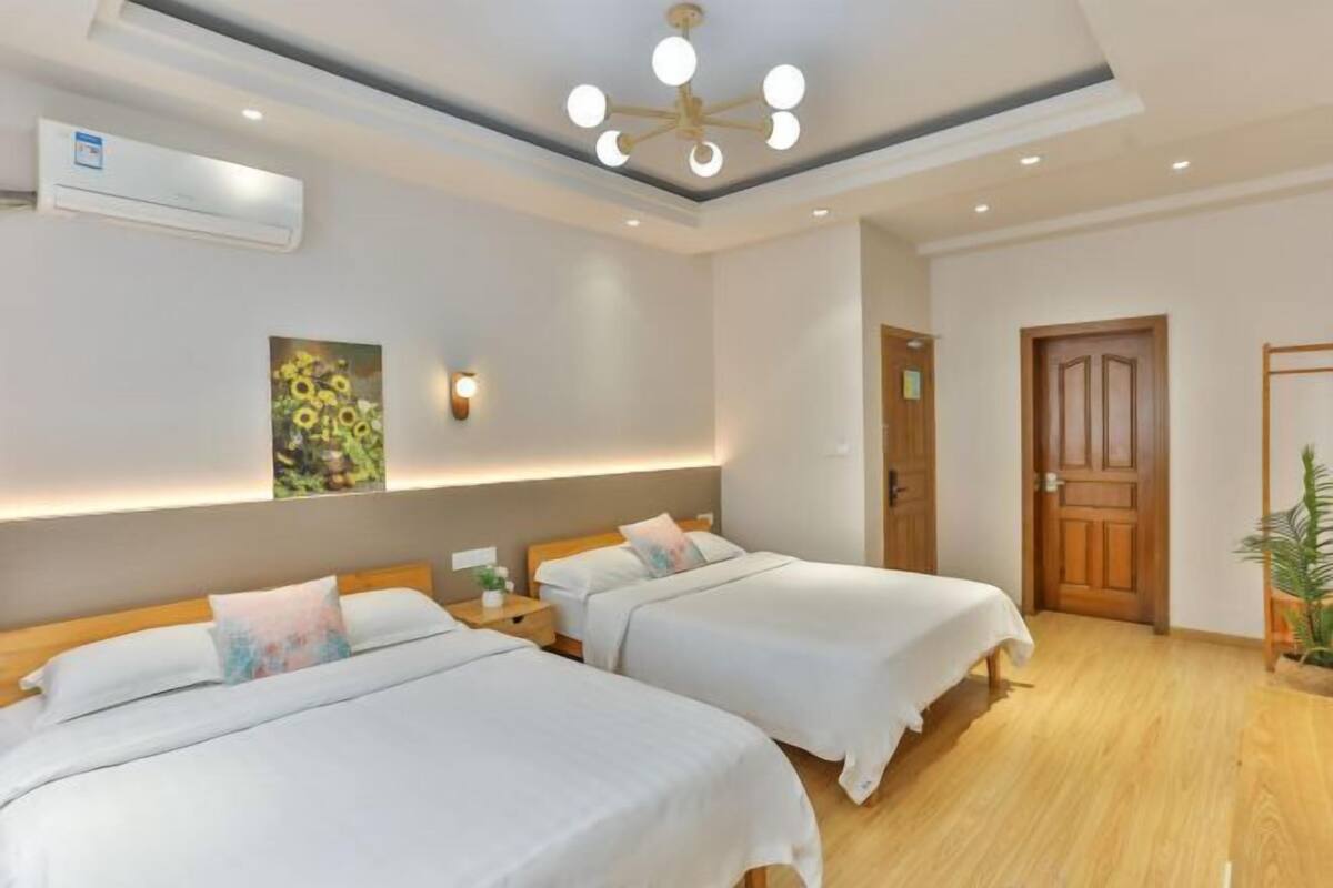 A hotel room with two beds, a ceiling fan, an air conditioning unit, a wooden door, and a wall-mounted light fixture.