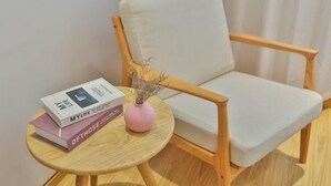A wooden chair with a white cushion, a small round wooden table with a pink vase and books, and a curtain in the background. - The 2 90's Guys Inn (Tongxiang)