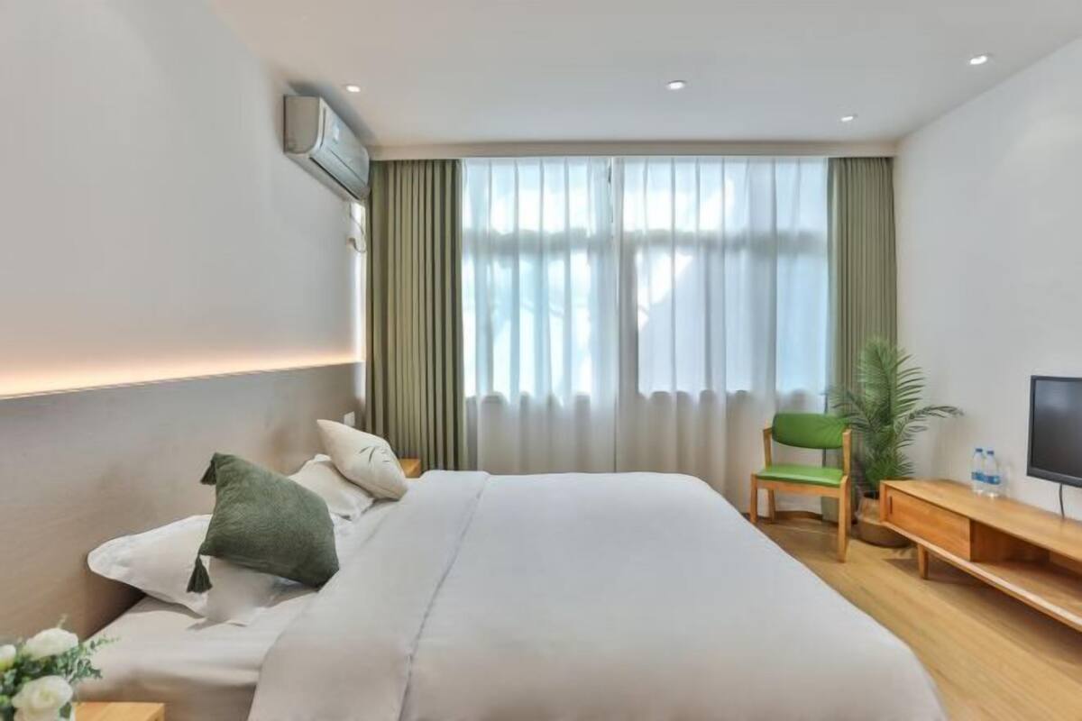 A hotel room with a large bed, a desk with a chair, a TV, and a window with curtains.
