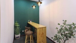 A small dining area with a wooden table and two bar stools, a green accent wall, and hanging pendant lights. - The 2 90's Guys Inn (Tongxiang)