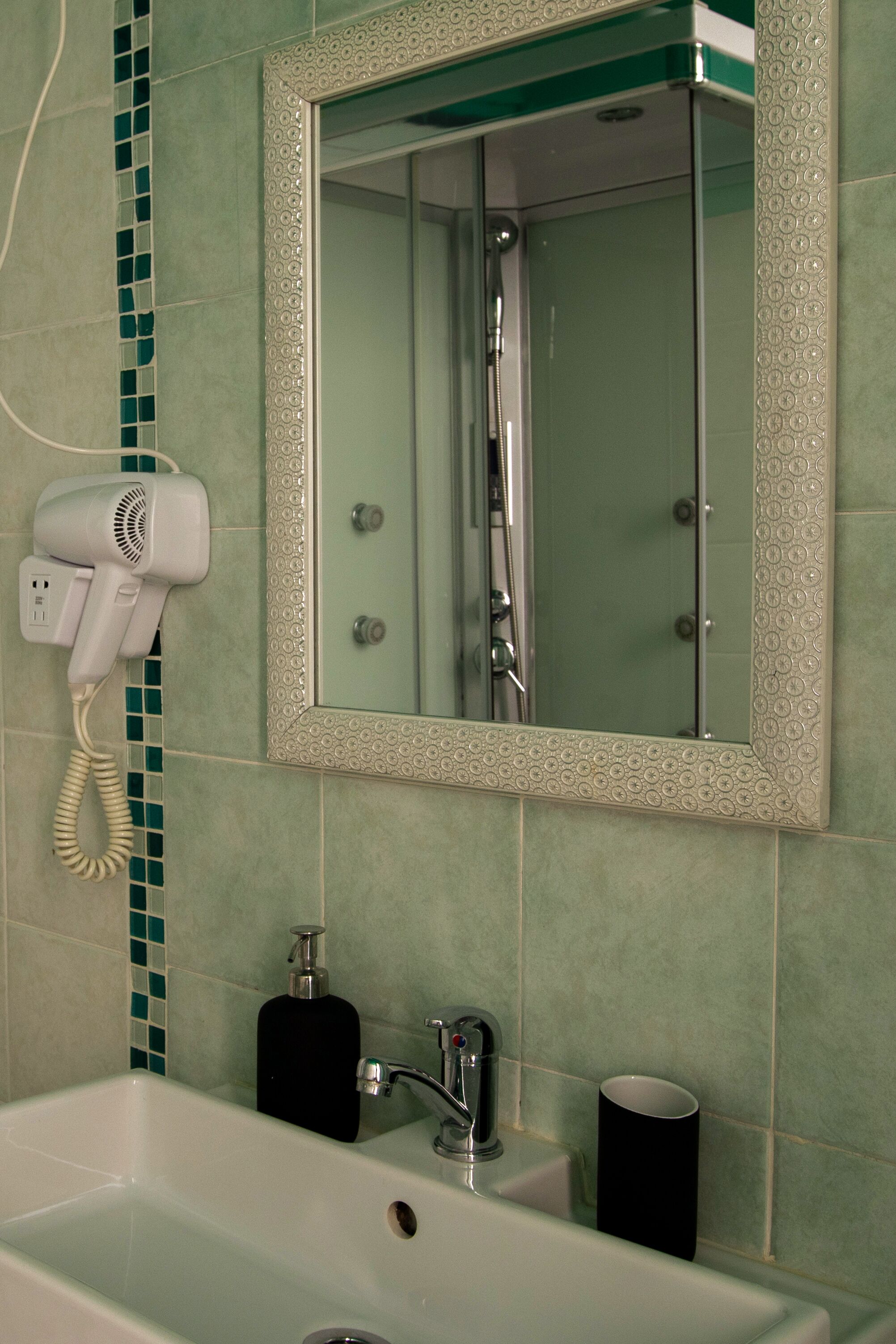 Un baño con un lavamanos blanco, un espejo y un secador de pelo montado en la pared.