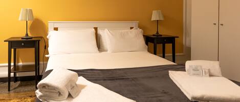 Een hotelkamer met een bed, twee nachtkastjes met lampen, een garderobe en netjes opgevouwen handdoeken op het bed.
