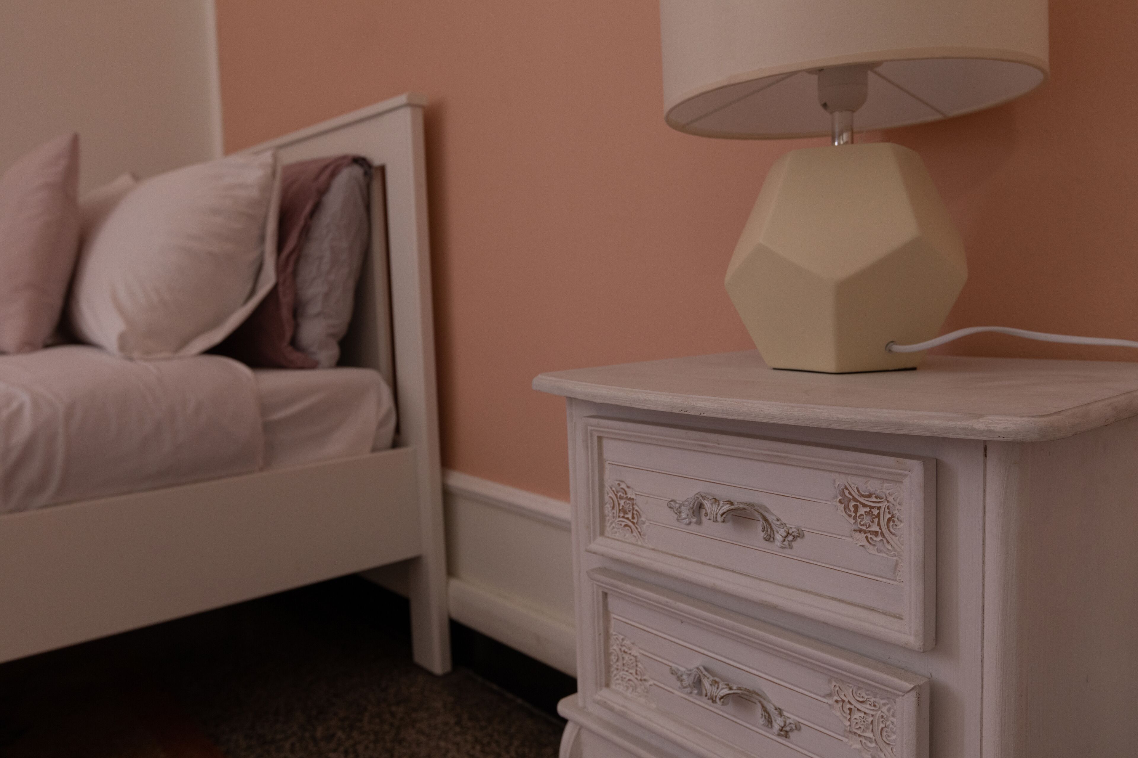 A bedroom with a bed, a nightstand with drawers, and a lamp.