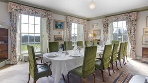 A dining room with a round table set for six, surrounded by green upholstered chairs. - Halecat House - Large Georgian House with Garden (Dog-friendly). (Witherslack)