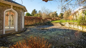 A stone pathway leading to a building with a white door and a window with a decorative glass design. - Halecat House - Large Georgian House with Garden (Dog-friendly). (Witherslack)
