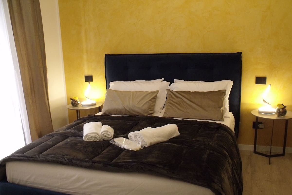 Ein ordentlich bezogenes Bett mit dunklem Kopfteil, zwei Nachttischlampen und auf jeder Seite ein kleiner Tisch mit einer Vase und einer Lampe.