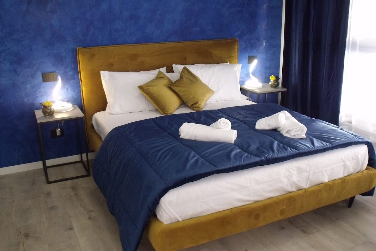 Ein Bett mit einer blauen und weißen Bettdecke, zwei Kissen und zwei gerollten Handtüchern.