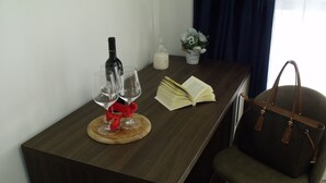 Een houten tafel met een wijnfles, twee wijnglazen, een boek, een vaas met bloemen en een handtas.