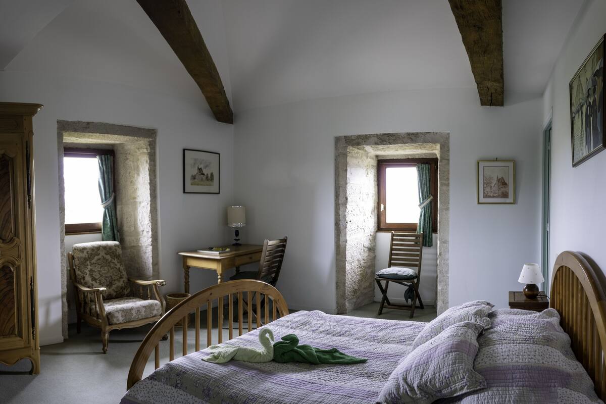 A bedroom with a bed, two chairs, a desk, and a lamp.
