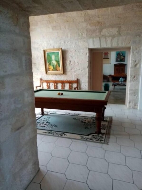 Una mesa de billar en una habitación con suelo de baldosas hexagonales y pared de piedra.
