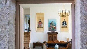 A room with a stone wall, a wooden sofa, a wooden cabinet, and a chandelier. - LA MAISON ROYALE (Pesmes)