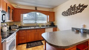 Una cocina con armarios de madera, encimera de granito, horno empotrado y ventana con persianas.