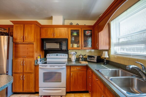 A kitchen with wooden cabinets, a stove, microwave, toaster, and a sink.