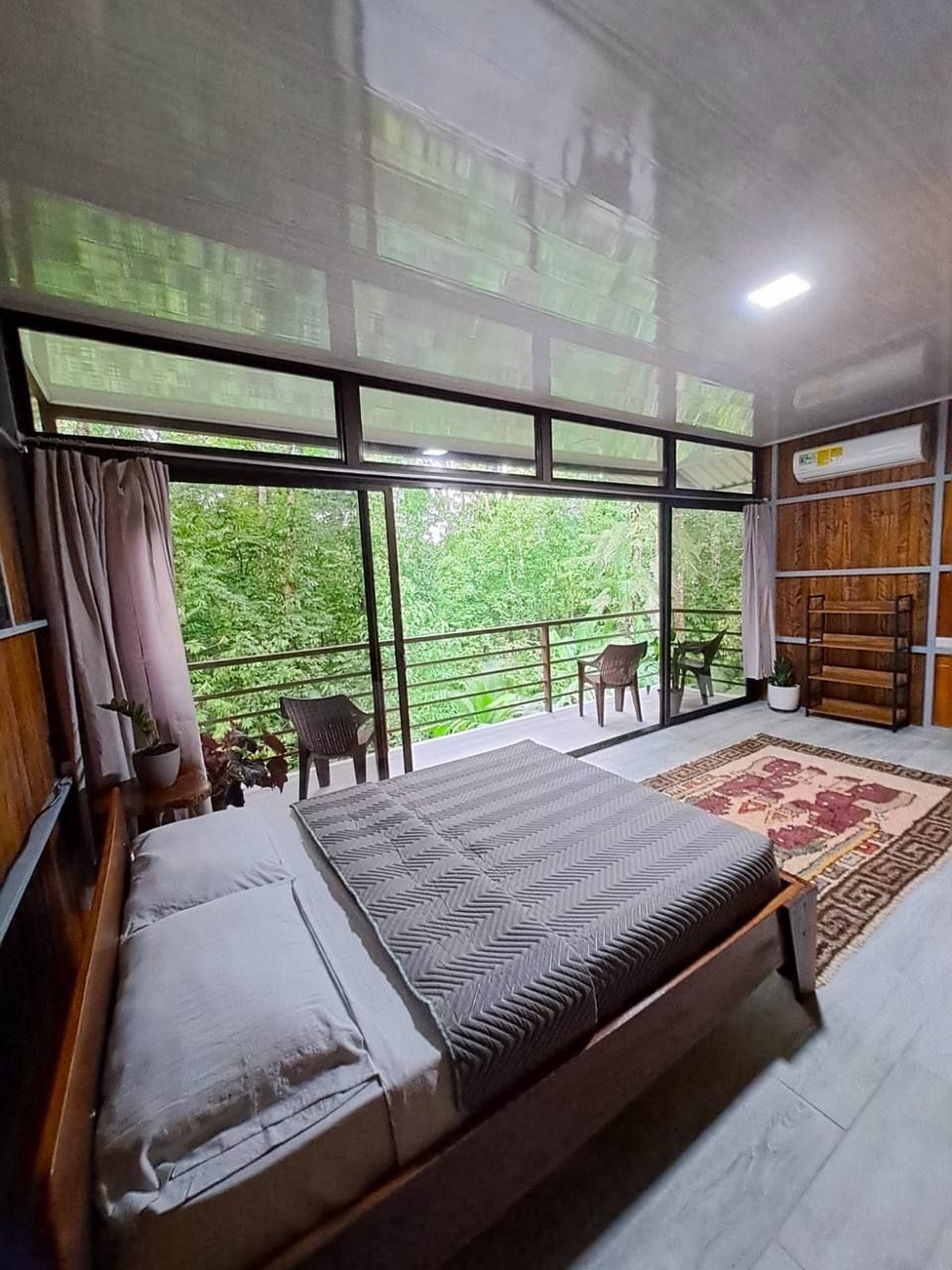 Une chambre avec un grand lit, un balcon avec des chaises et une vue sur la verdure.