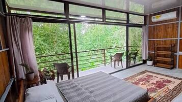 Une chambre avec un grand lit, un balcon avec des chaises et une vue sur la verdure.